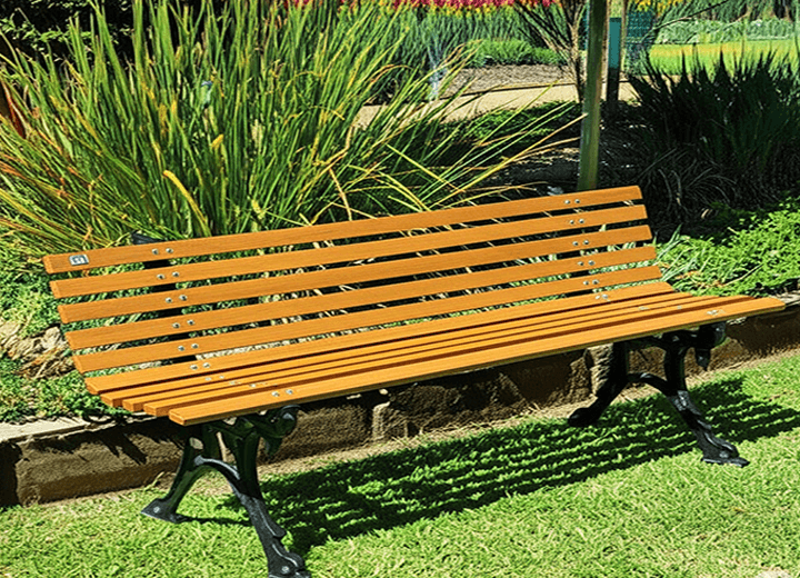 Banco de jardim de madeira com encosto posicionado em área externa com plantas ao redor
